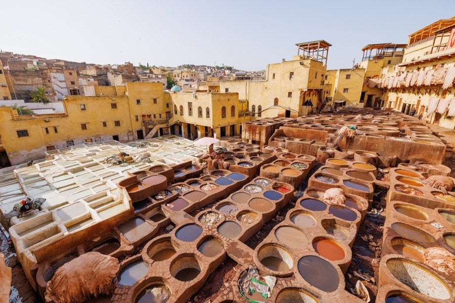 Las cubas de tinte de la curtiduría Chouara se extienden al aire libre, rodeadas por edificios tradicionales de adobe y pieles secándose bajo el sol en Fez.