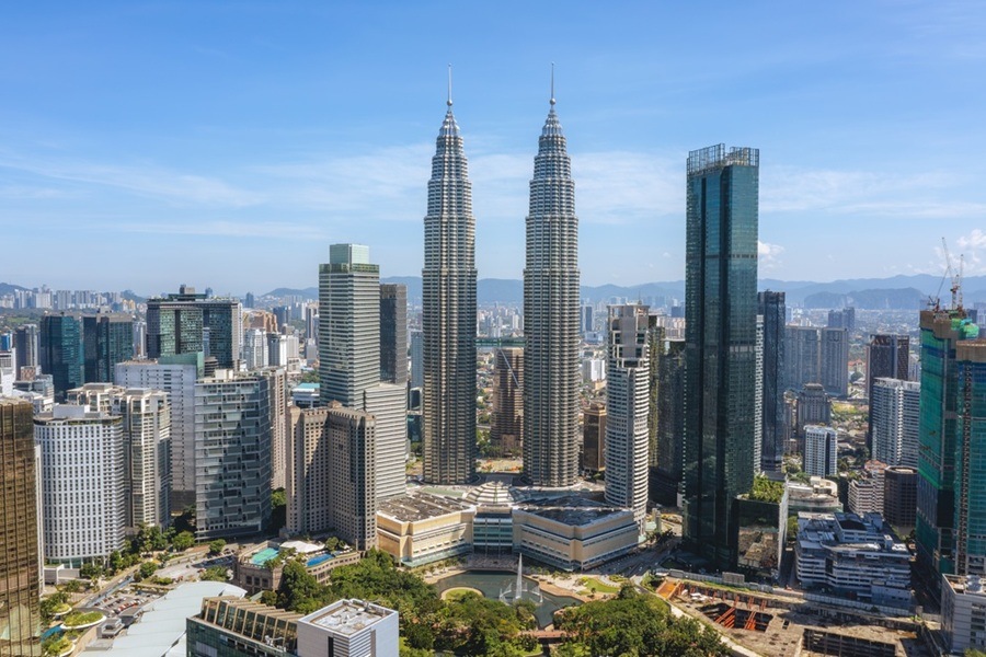 Las Torres Petronas se elevan majestuosas en el centro del horizonte urbano de Kuala Lumpur, rodeadas de rascacielos y áreas verdes bajo un cielo despejado.