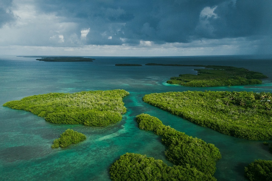 Extensas islas de manglares verdes se extienden dividiendo canales de agua turquesa y cristalina, bajo un cielo nublado y tormentoso que se proyecta sobre el horizonte marino.