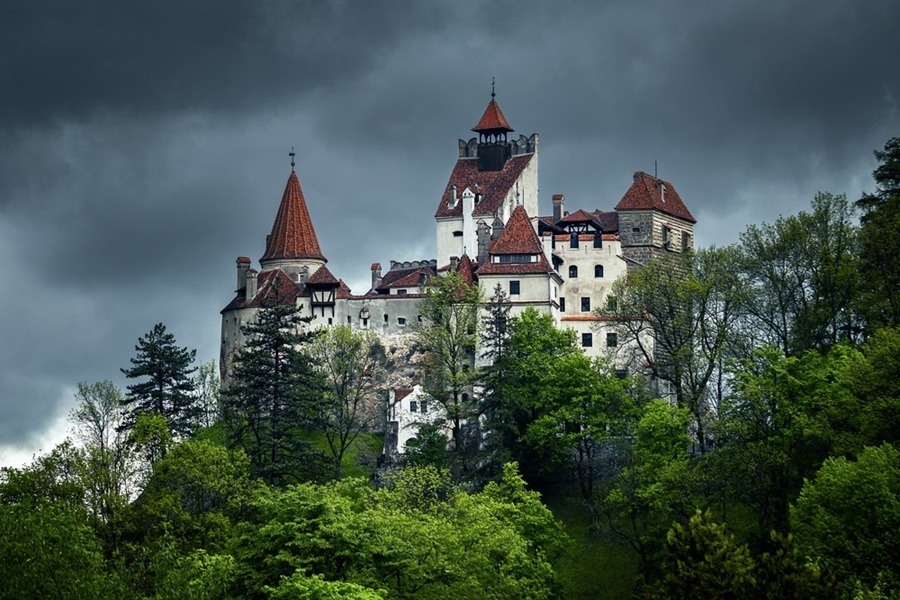El Castillo de Bran se erige sobre un promontorio rocoso, rodeado de frondosos árboles verdes y bajo un cielo plomizo y tormentoso.