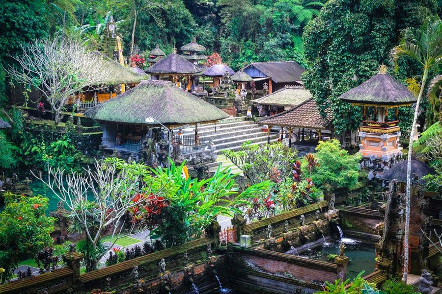 Varias santuarios y pavellones de techo de paja del templo Gunung Kawi Sebatu reposan entre frondosa vegetación tropical, jardines y estanques de agua en Bali.