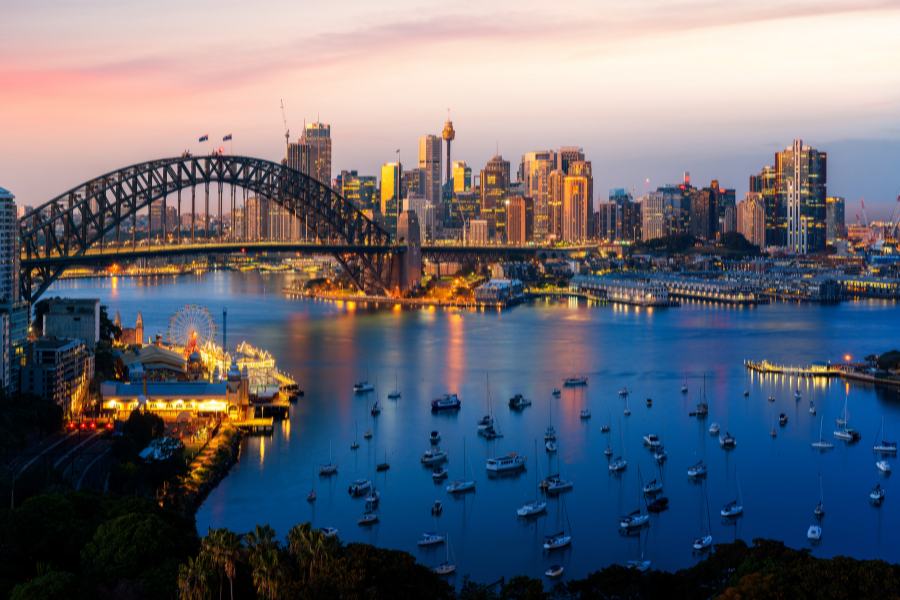 vista aerea del puente harbour uno de los monumentos más visitados en australia con barcos alrededor en el mar y la ciudad iluminada de fondo en un atardecer rojizo