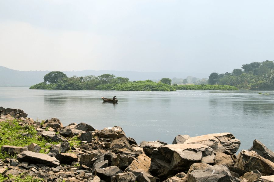 Lago Victoria: Paisaje sereno del lago Victoria con frondosa vegetación en las orillas y rocas sobresaliendo de las aguas tranquilas.