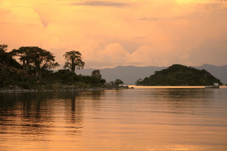Lago Malaui: Atardecer dorado sobre las tranquilas aguas del lago Malaui con siluetas de islas y árboles en el horizonte.