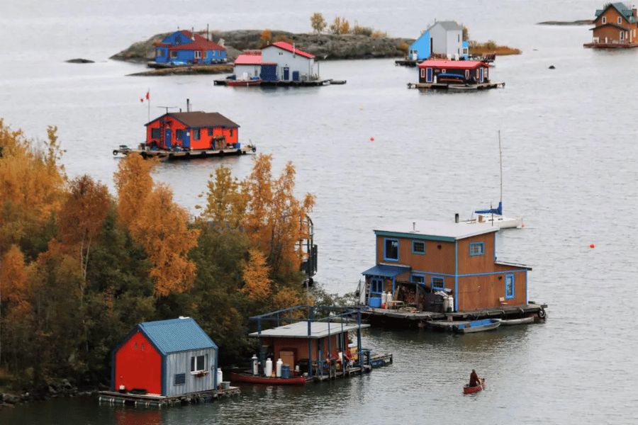 Gran Lago del Esclavo: Casas flotantes coloridas amarradas a lo largo de la orilla arbolada del Gran Lago del Esclavo en otoño.