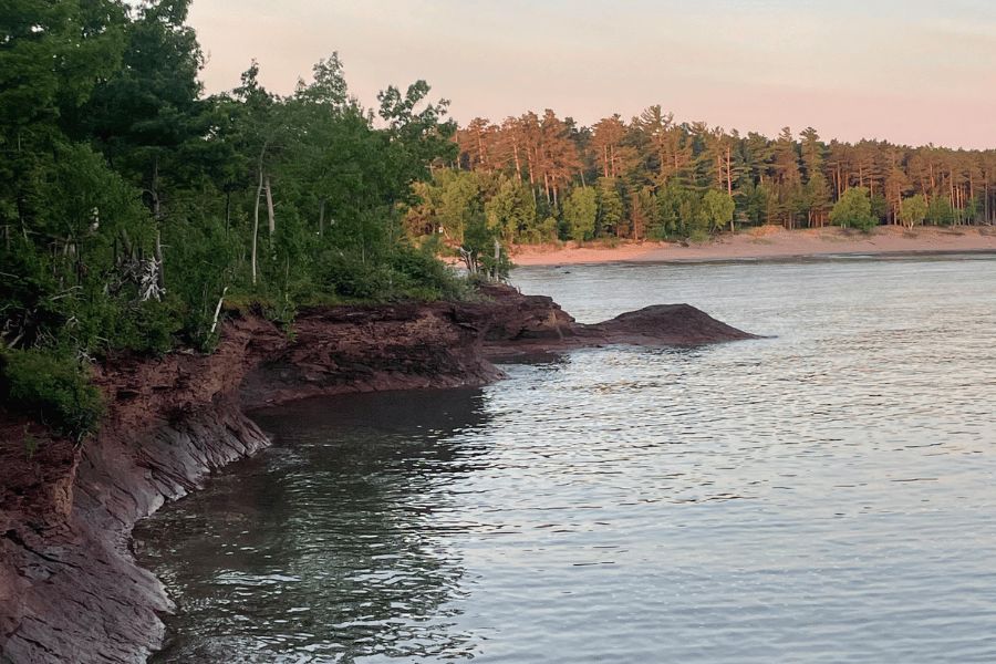 Lago Superior: Acantilados de tierra rojiza bordeando las frías aguas del lago Superior junto a un bosque.