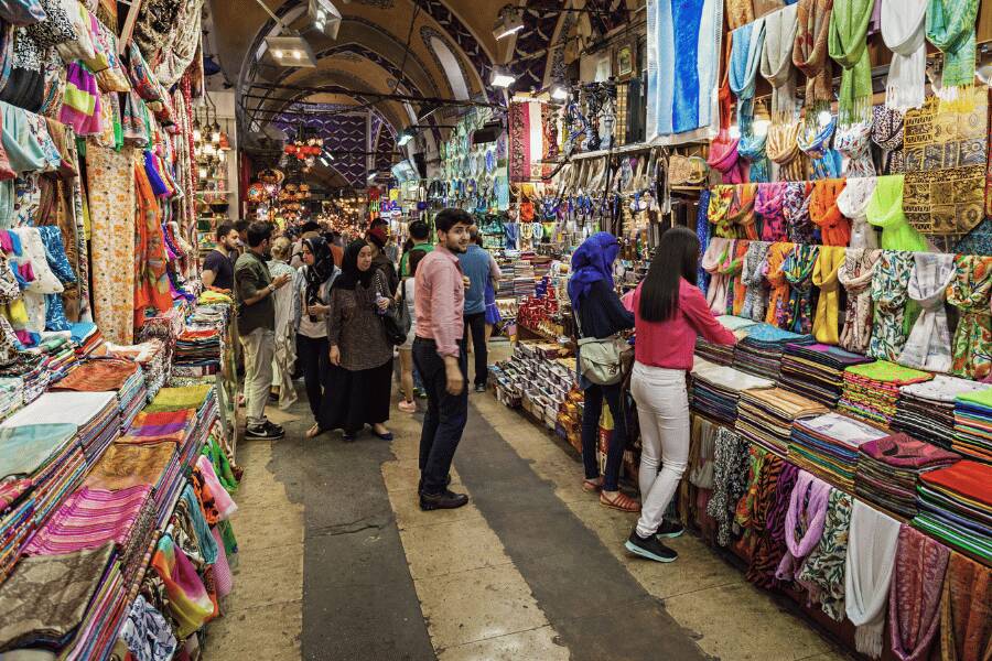 Compradores caminan por un pasillo cubierto rodeado de tiendas llenas de textiles y artesanías coloridas. Gran Bazar, Turquía