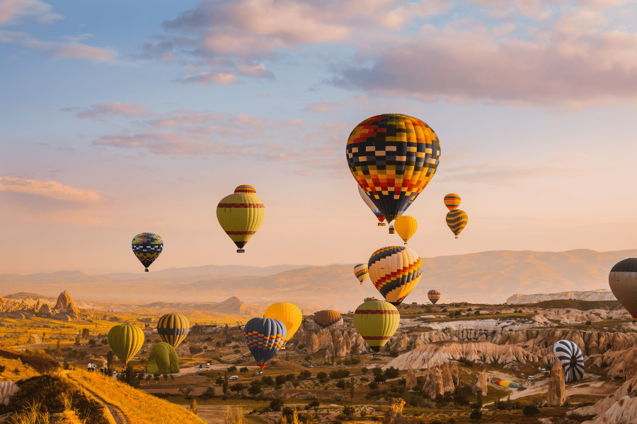 Varios globos aerostáticos flotan sobre el paisaje rocoso de Capadocia, Turquía, durante el amanecer bajo un cielo parcialmente nublado.