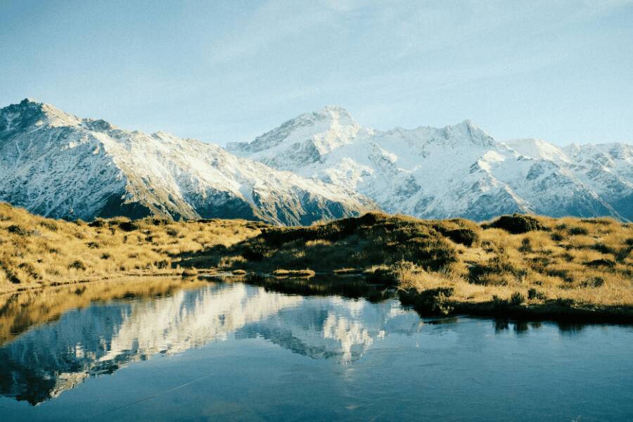 Montañas nevadas se reflejan en la superficie tranquila de un lago rodeado de colinas doradas en nueva zelanda