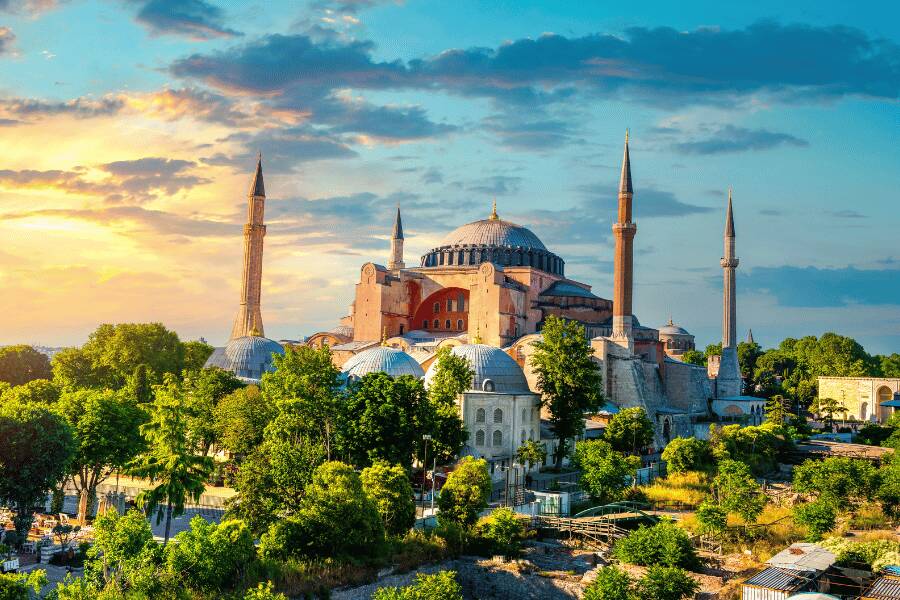 La mezquita de Santa Sofía en Estambul, Turquía, se alza con sus minaretes y cúpulas rodeada de árboles y vegetación bajo un cielo al atardecer.