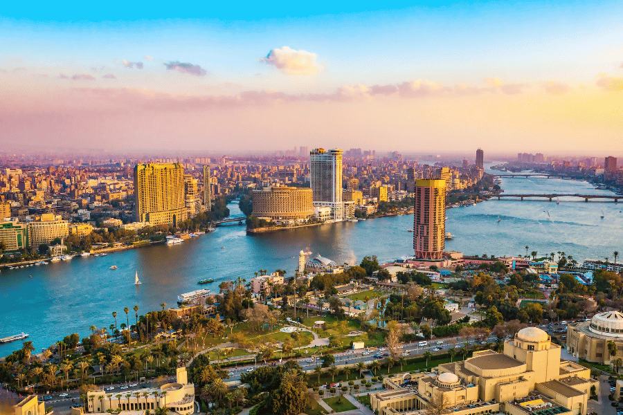 Ciudad de El Cairo, Egipto vista desde el aire con cielo azul y rosa y nubes, edificios altos estilo rascacielos y el río Nilo cruzando la ciudad con barcos y puentes a lo lejos