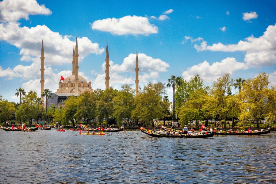 Río Nilo en la ciudad de Aswan, Egipto con barcos de colores y personas subidas, rodeados de árboles verdes y un cielo azul con nubes