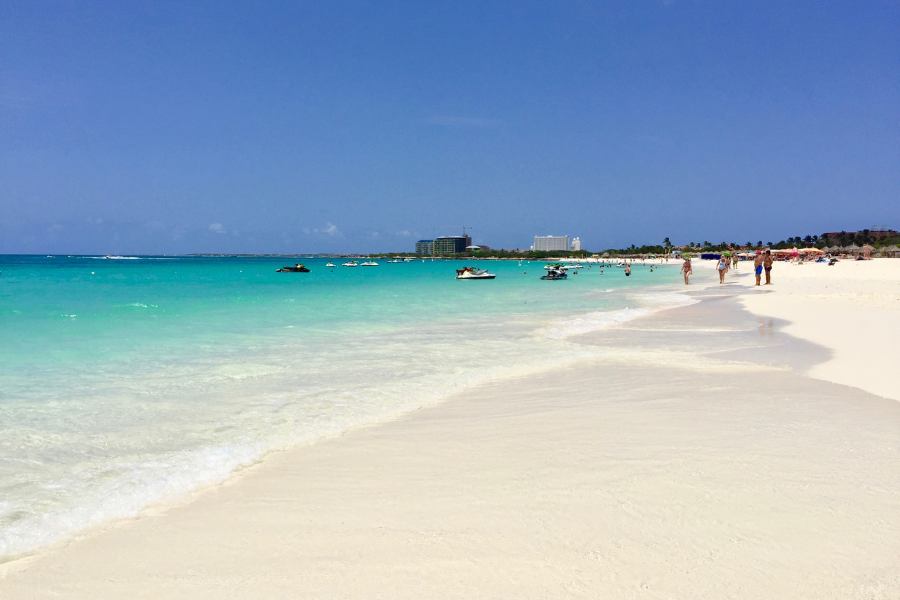Playa Eagle Beach en Aruba con su característica arena blanca fina y los icónicos árboles Fofoti inclinados hacia el mar turquesa del Caribe.