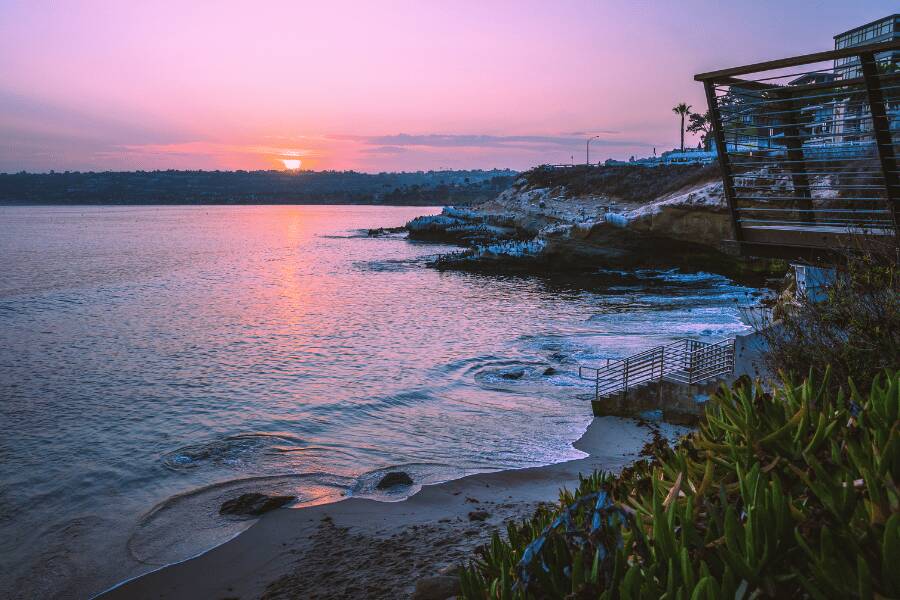 La Jolla: Olas rompiendo contra la costa rocosa durante un atardecer de tonos rosados en La Jolla, San Diego.