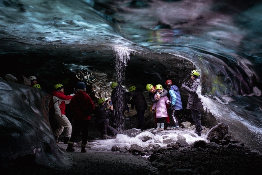 Un grupo de turistas con casco explora el interior de una cueva de hielo azul en el glaciar Vatnajökull, Islandia, mientras cae una pequeña cascada de agua sobre las rocas.