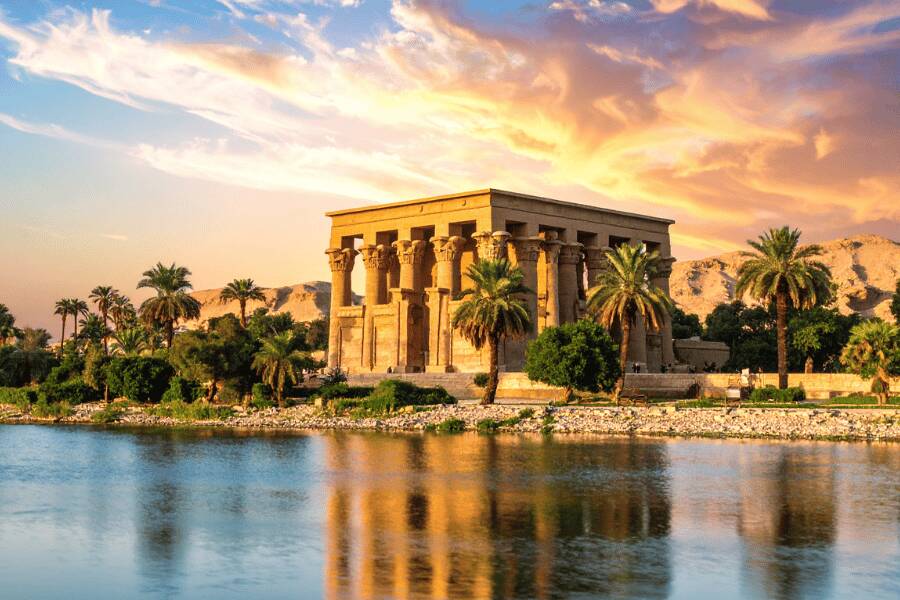 Templo de Isis, Egipto, atardecer con colores rojizos, delante del agua y con palmeras que rodean el templo