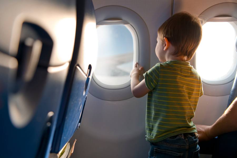 Un niño con camiseta de rayas mira por la ventanilla de un avión en el interior de la cabina de pasajeros iluminada por el sol de la tarde.