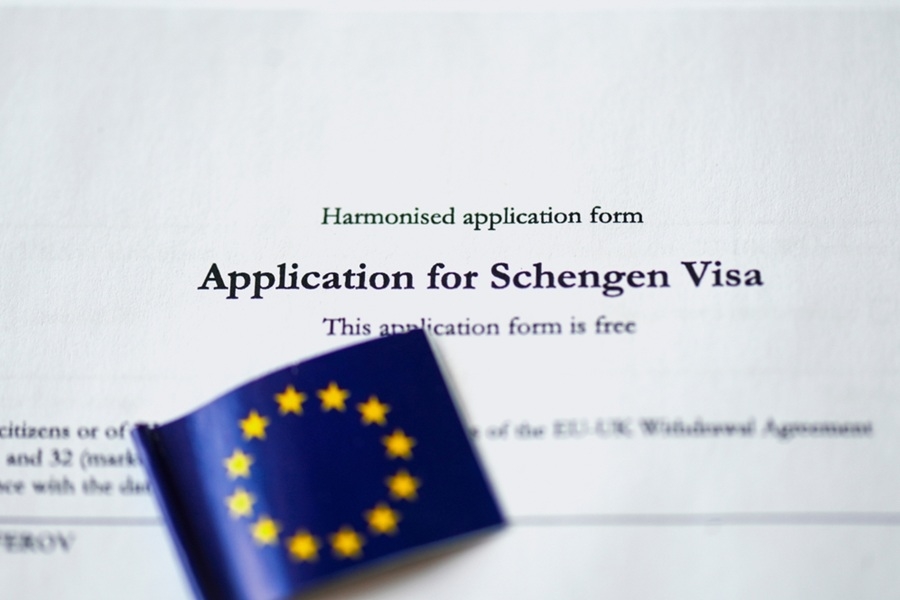 Una pequeña bandera de la Unión Europea reposa sobre un formulario oficial de solicitud impreso en papel blanco. Texto en la imagen: "Harmonised application form", "Application for Schengen Visa", "This application form is free".