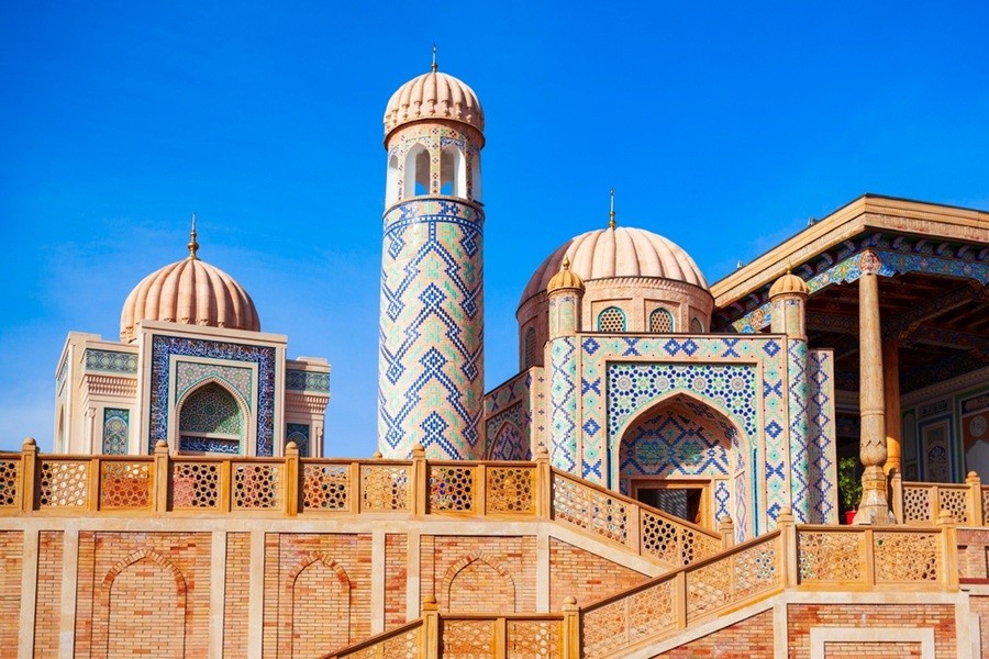 Estructura decorada de la mezquita Hazrat Khizr con un minarete labrado, cúpulas estriadas en tono beige y portadas azulejadas sobre una terraza elevada de ladrillo en Samarcanda, Uzbekistán.
