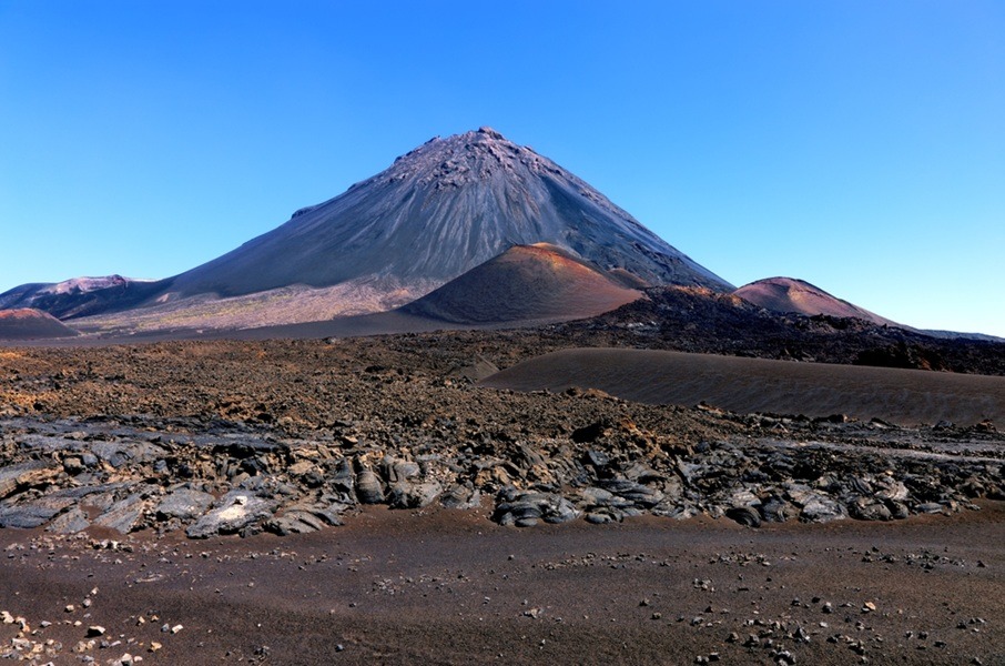 Imponente cono volcánico del Pico do Fogo elevándose sobre un vasto e árido campo de lava negra bajo un cielo azul despejado en Chã das Caldeiras, isla de Fogo, Cabo Verde.