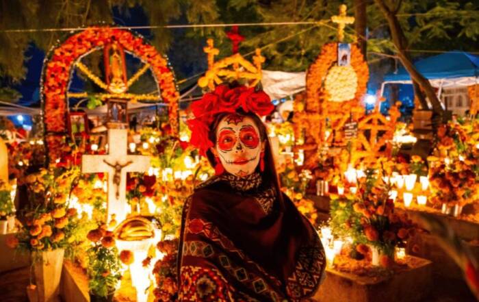 mujer con la cara pintada de catrina en dia de muertos, méxico, rodeada de velas, cruces y ofrendas a los muertos