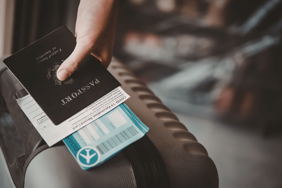 Mano sosteniendo un pasaporte y una tarjeta de embarque sobre una maleta de viaje en el interior de una terminal.